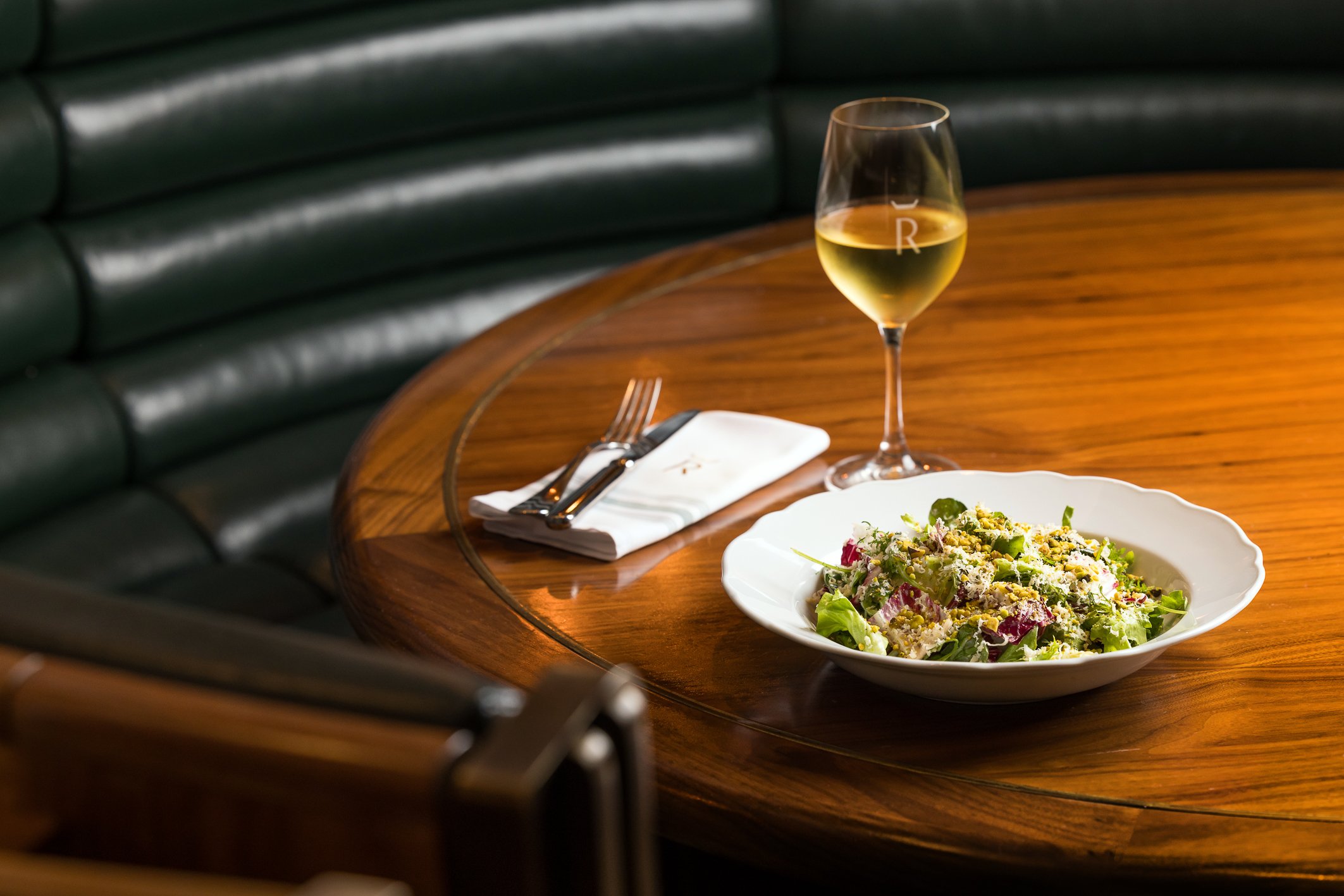 A table at Reign Restaurant with a bowl of salad and glass of white wine.