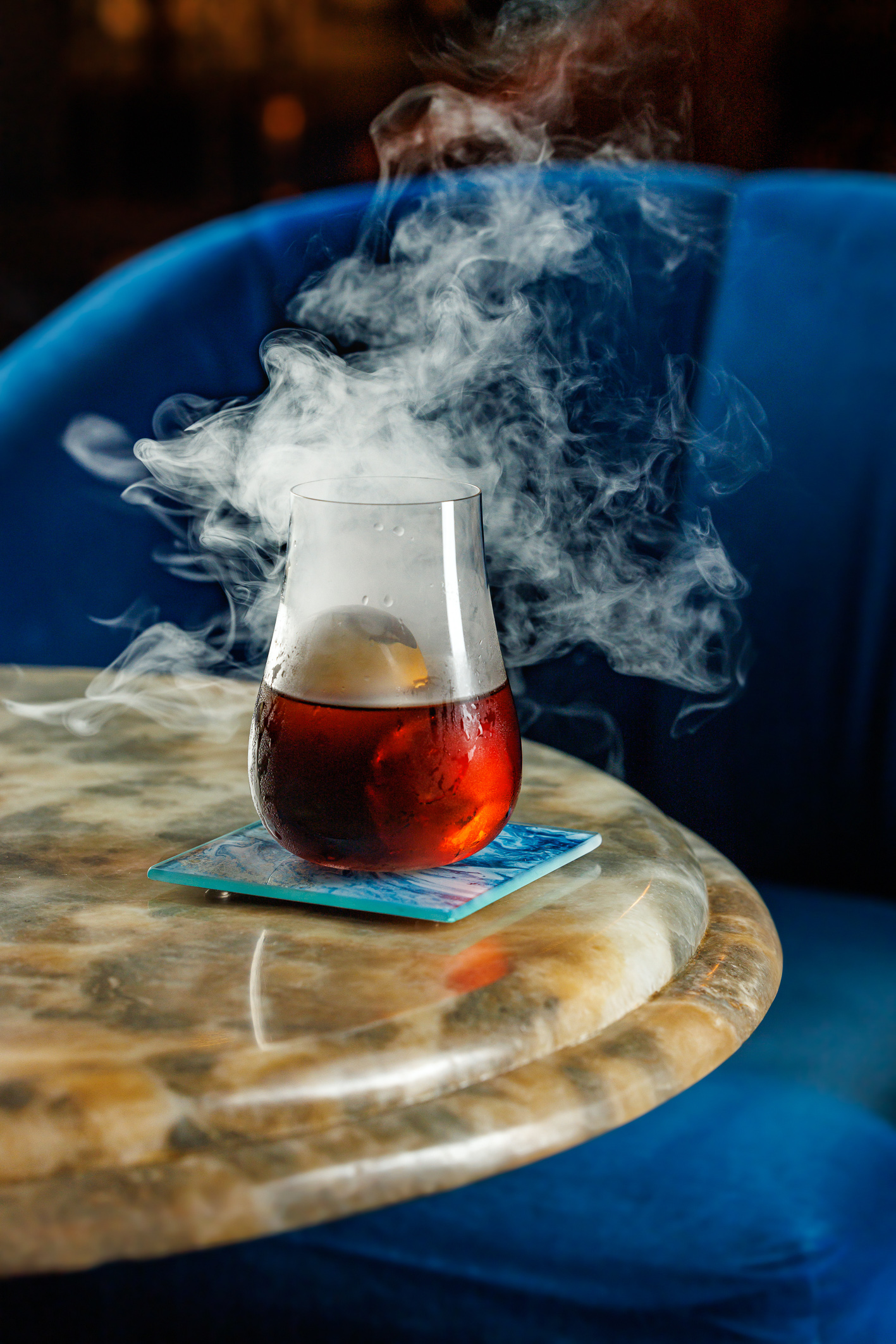 A red cocktail in a smokey glass on marble bar table.