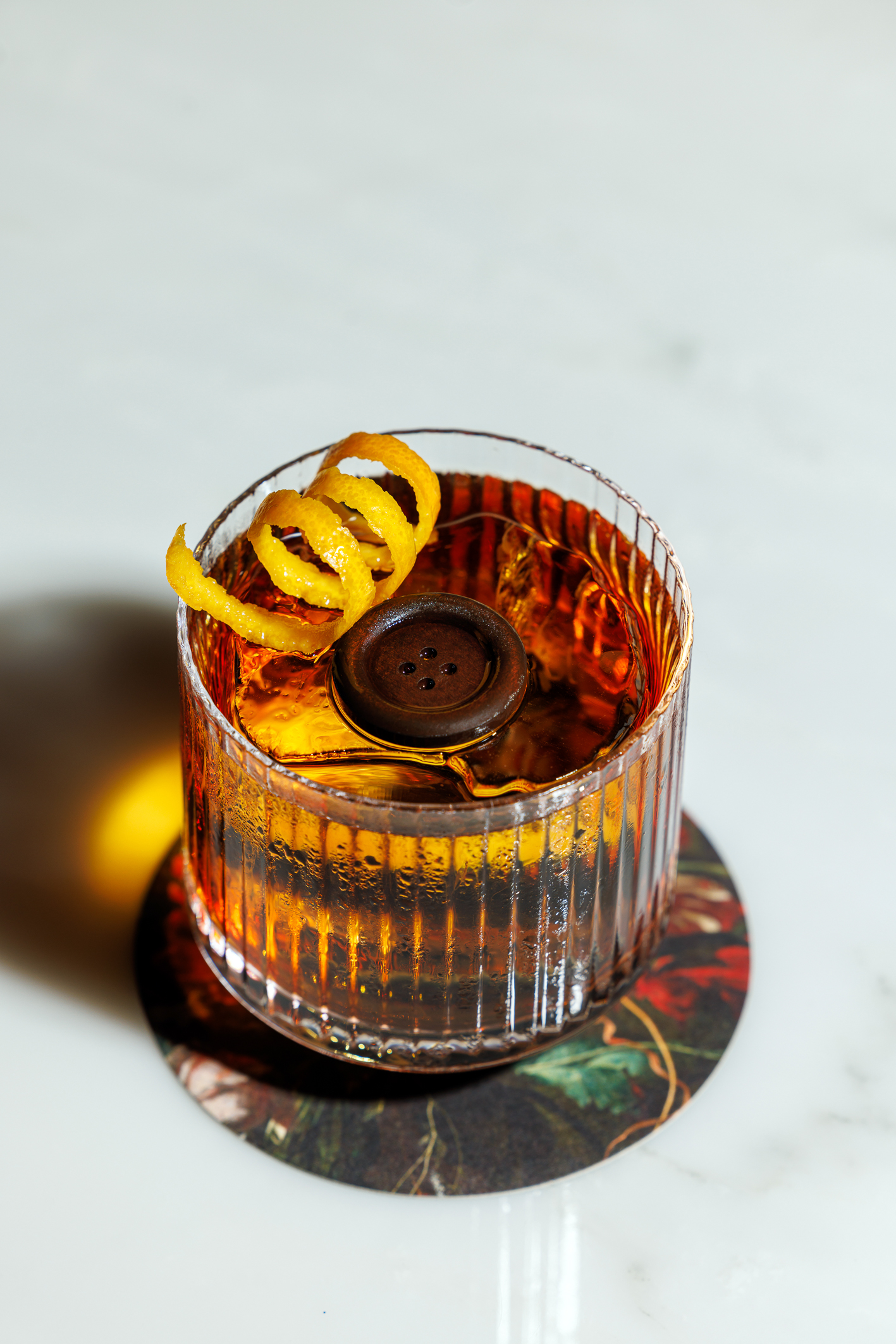 A button floating in an orange cocktail with a curled lemon rind garnish