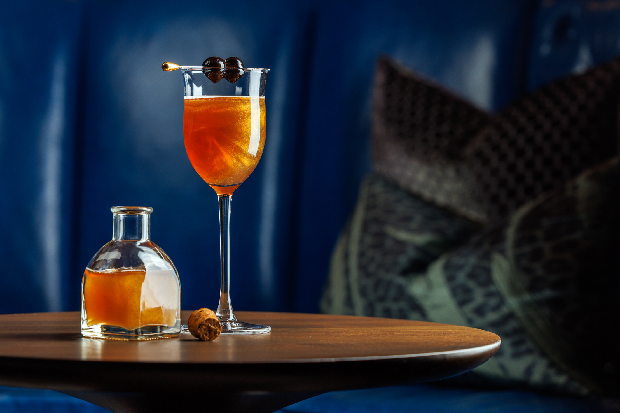 A tall glass and a glass decanter filled with an amber coluored cocktail.