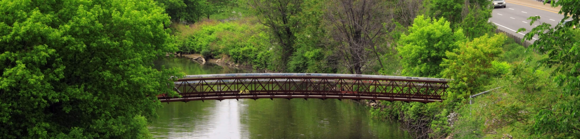 A walking bridge over a river next to a highway.