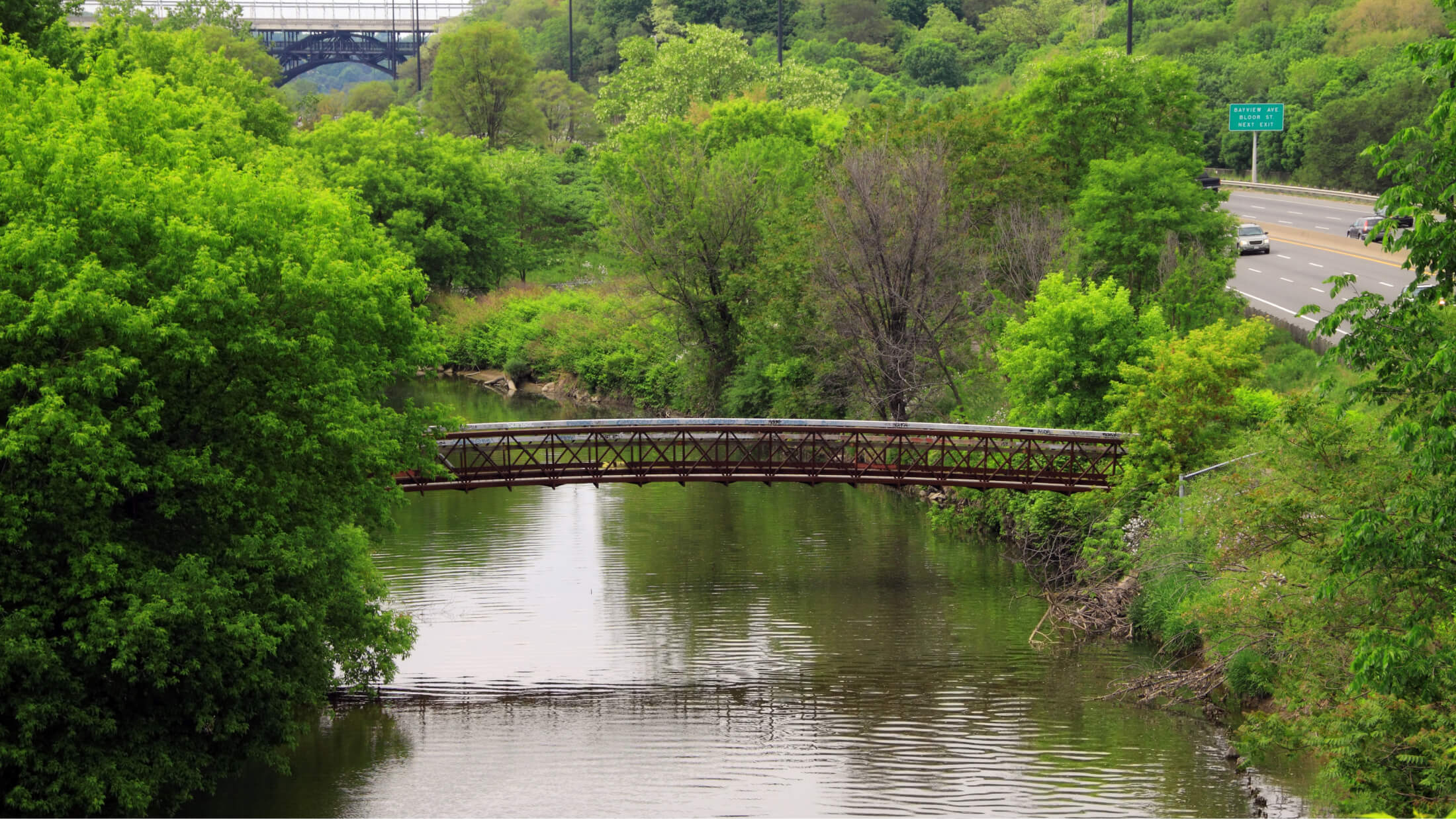 A walking bridge over a river next to a highway.