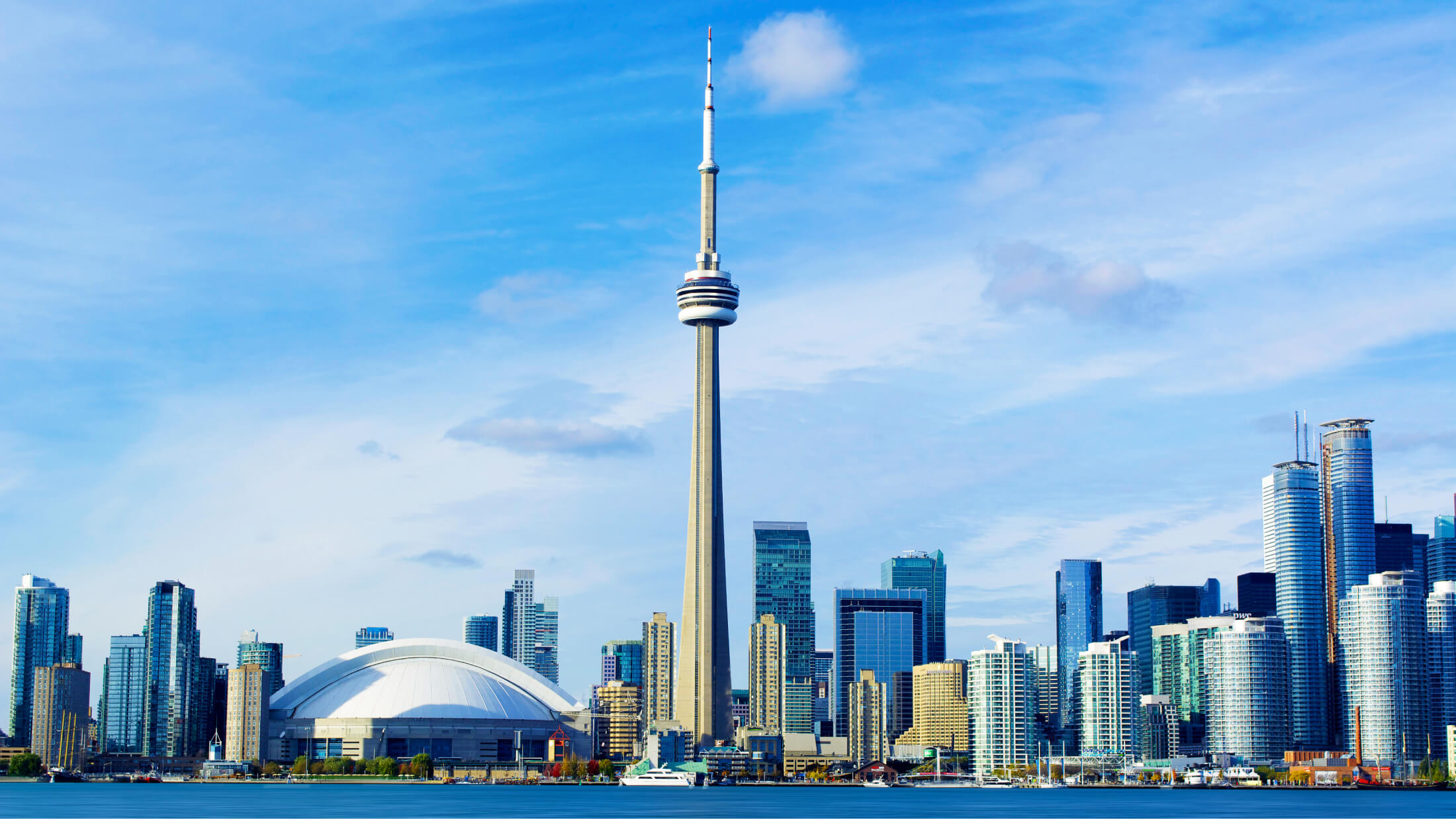 The CN Tower and Rogers stadium in the Toronto skyline on a clear blue-skied day.