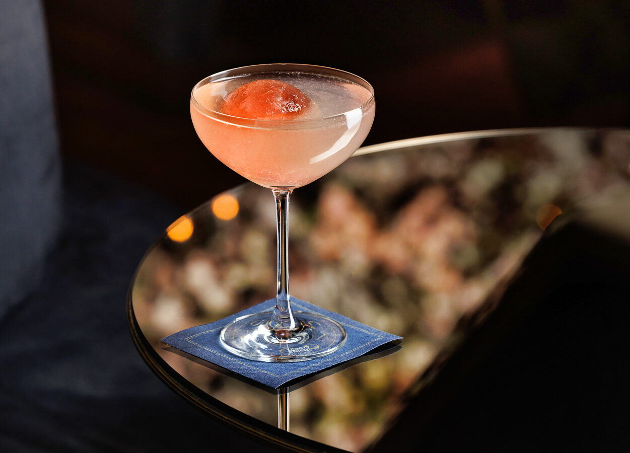A pink cocktail in a champagne coupe with a ball of pink ice in the center.